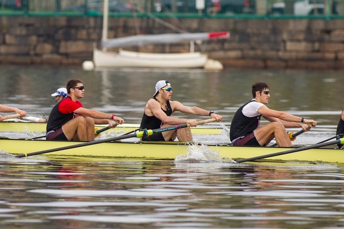 Northeastern men's rowing team practices rowing in a river on a sunny day.