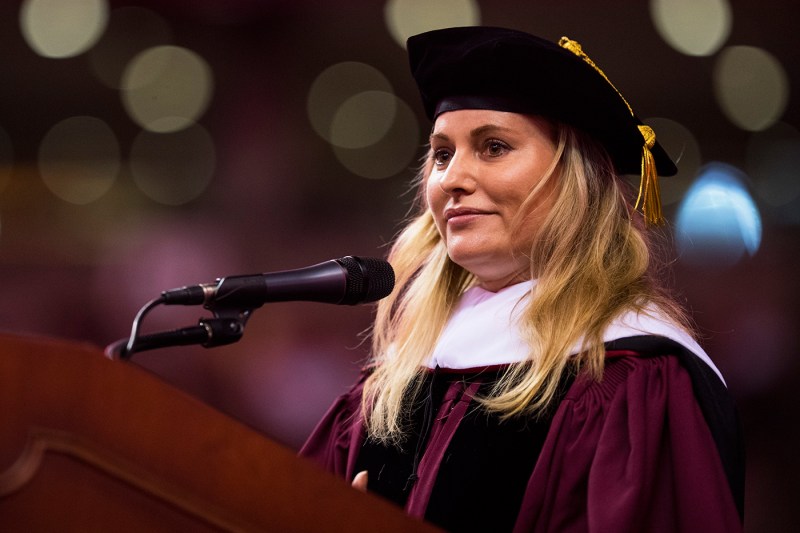 Aimée Mullins in Commencement regalia, speaking at the podium