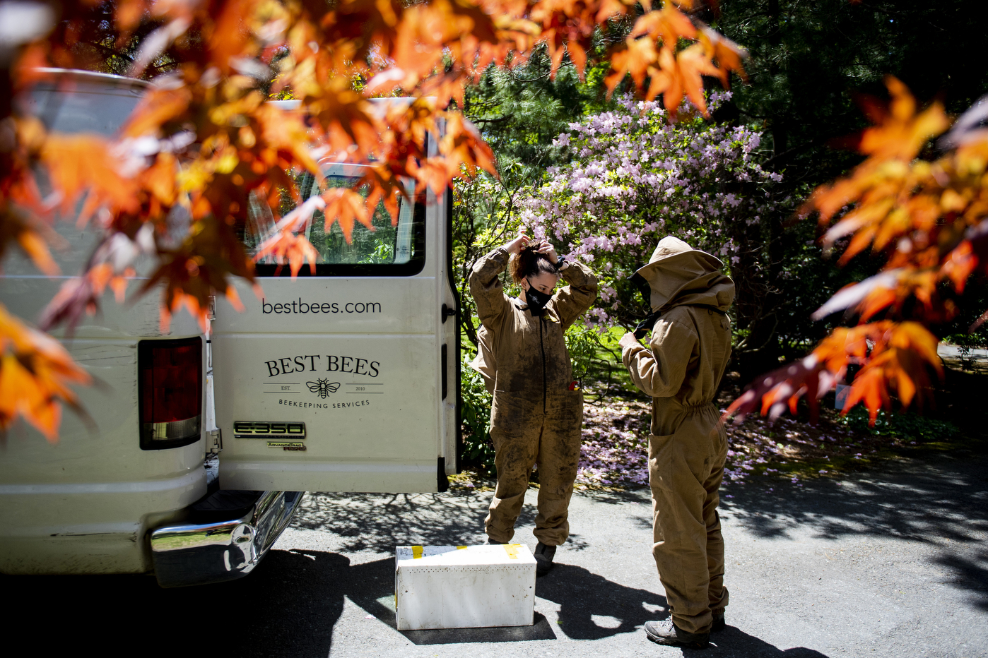 Two beekeepers suit up next to a van