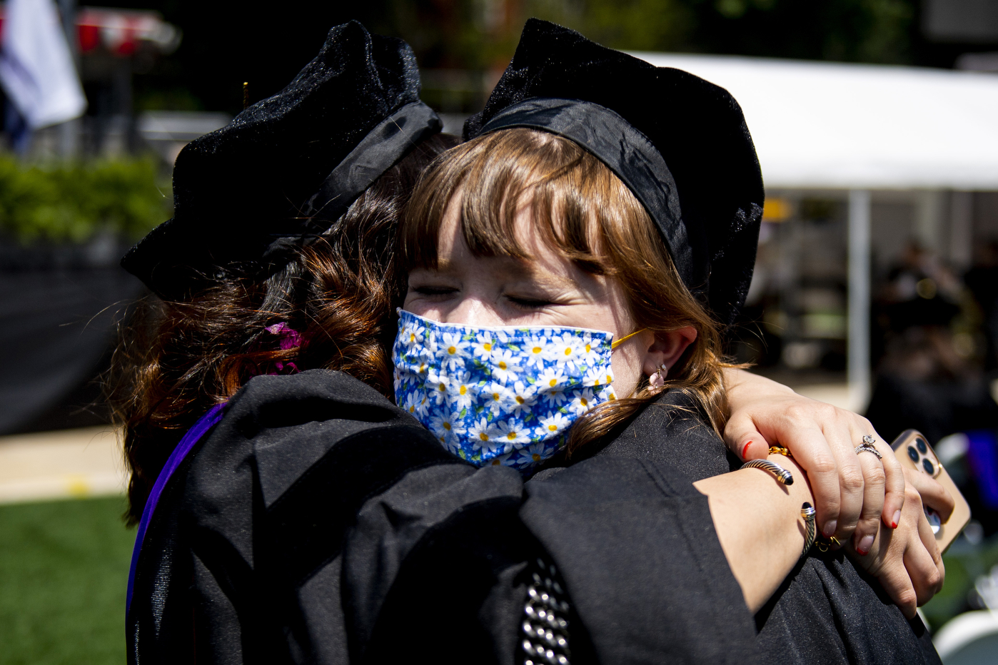 Masked students in caps and gowns hugging.