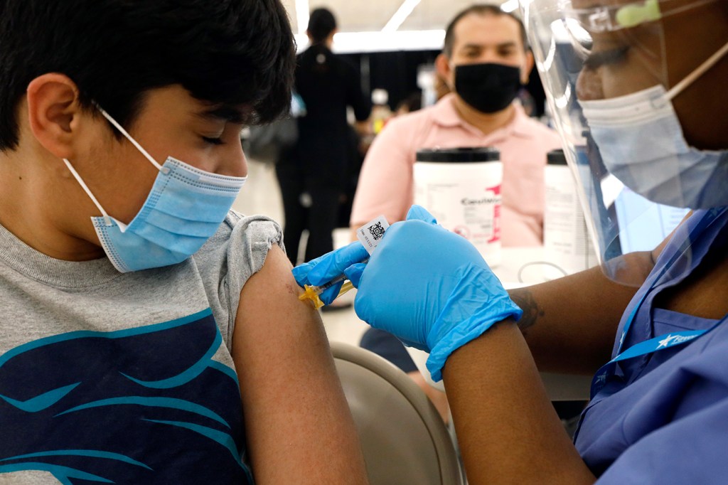 Shivam Patel, 13, receives his first Pfizer COVID-19 vaccination from nurse Diawna Jenkins as his father, Rajesh Patel, observes from the background at the Cook County Public Health Department on May 13, 2021, in Des Plaines, Ill. AP Photo by Shafkat Anowar