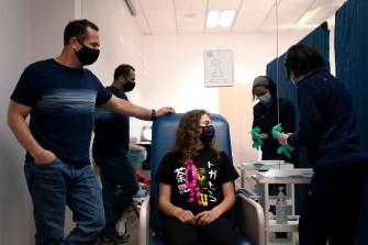 Daughter waits to get vaccinated while her father stands nearby