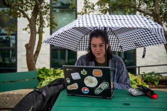 northeastern student using laptop while holding umbrella