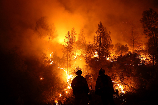 silhouettes of two firefighters standing in front of massive wilfdire