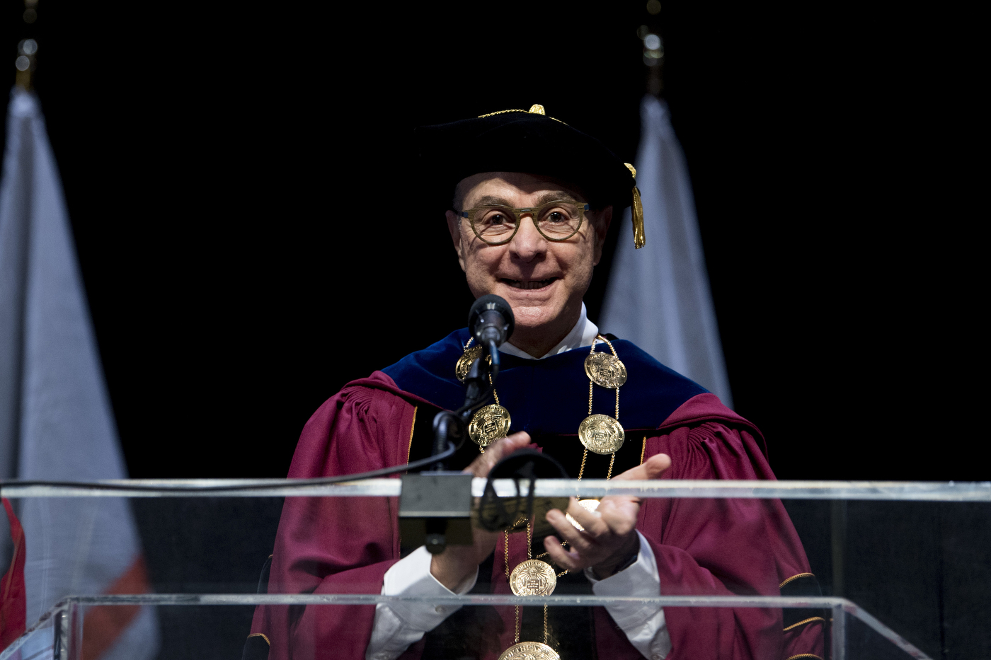 A man in academic regalia smiles and claps