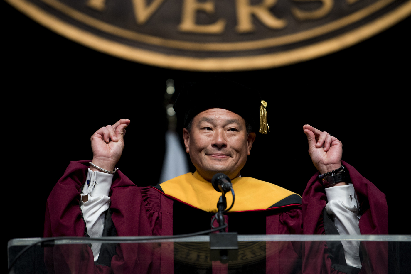 A man in academic regalia raises his hands in celebration