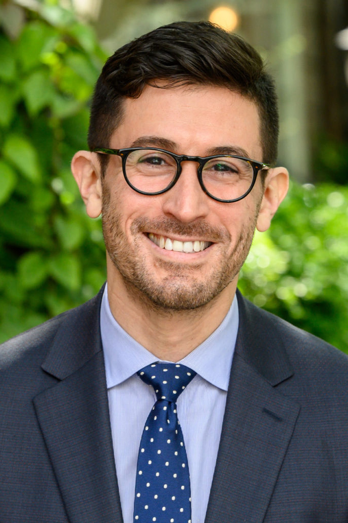 dark haired man with glasses wearing suit and tie