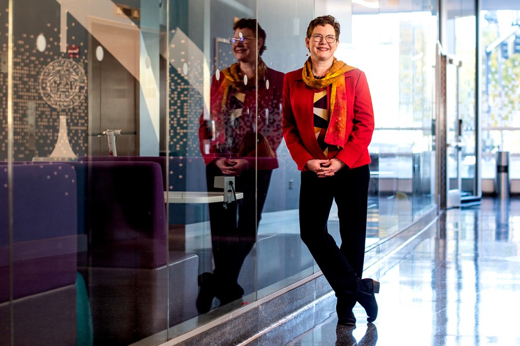 woman leaning against glass wall wearing red blazer and orange scarf