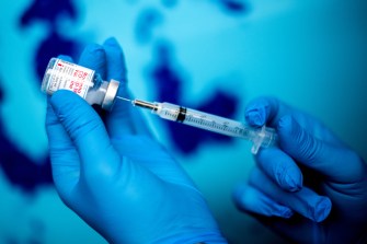 gloved hands filling a syringe with moderna covid vaccine