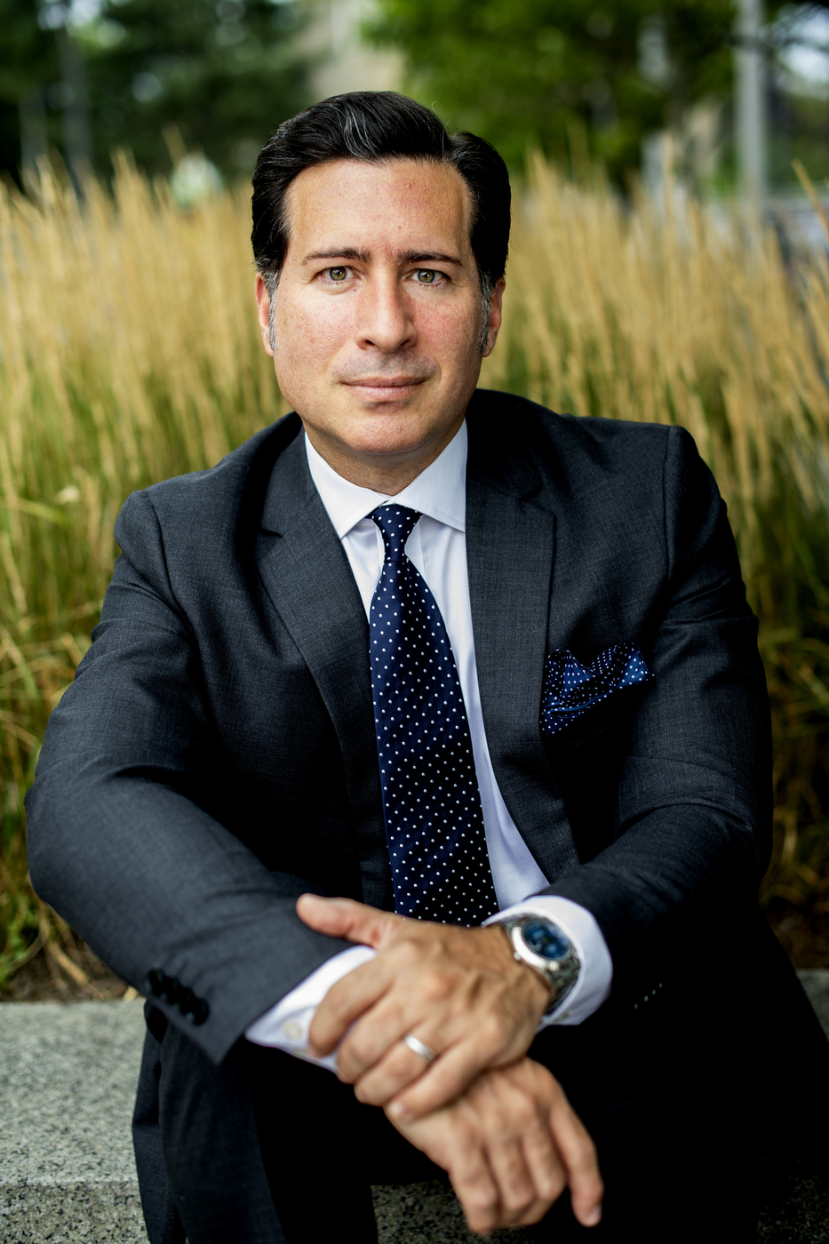 man wearing suit and tie sitting in front of long grass