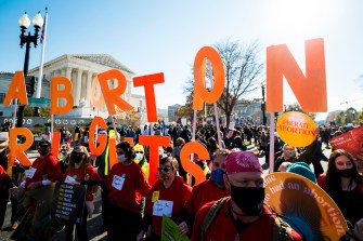 protestors stand outside supreme court building holding orange letters that spell abortion rights