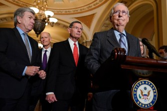 Senate Minority Leader Mitch McConnell stands behind a podium at a press conference inside of a room in Washington with Sen. Roy Blunt, Sen. Rick Scott, Sen. John Barrasso, and Sen. Joni Ernst standing behind him.