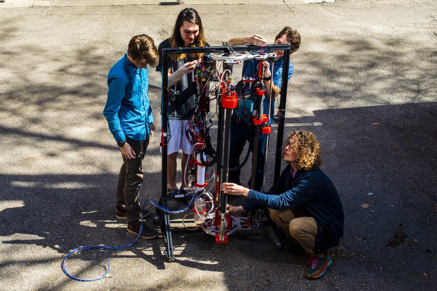 Four students evaluate and adjust a thin, rectangular machine