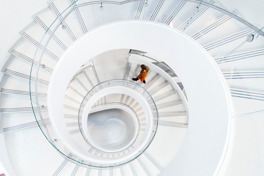 A person walks down a white spiral staircase.