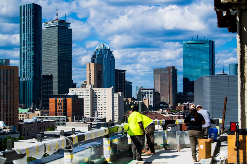 members of the northeastern community stand on the roof of the exp building with downtown boston in the background