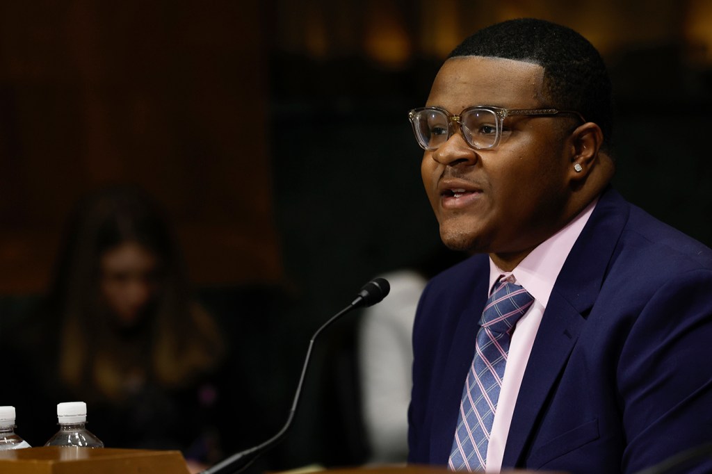 young man wearing a suit and glasses in front of a mic