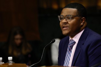 young man wearing a suit and glasses in front of a mic