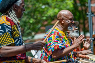 black men playing the drums wearing colorful shirts