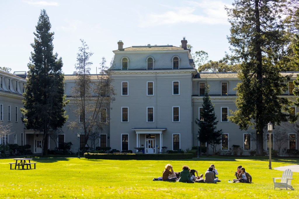 large white building with green lawn and pine trees in front of it