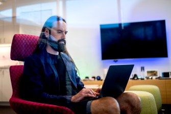 man with long hair sitting in red chair with laptop on his lap