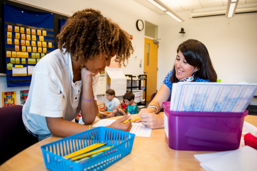 a teacher points to a piece of paper while teaching a student to read