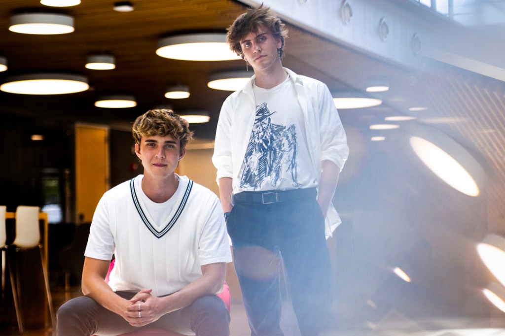 two students wearing white shirts, one sitting on the left and one standing on the right