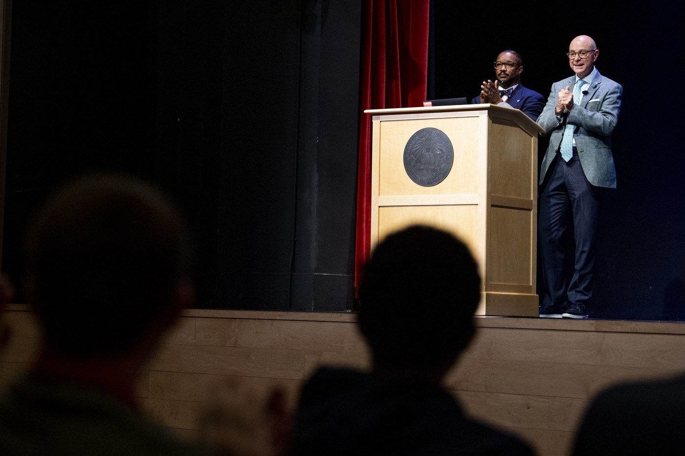 Two speakers standing on a stage clapping