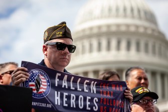 man holding a blue banner that says fallen heroes in all caps on it