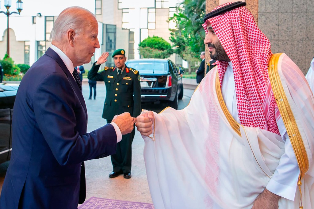 older man wearing blue suit fist bumping man wearing traditional arabic dress