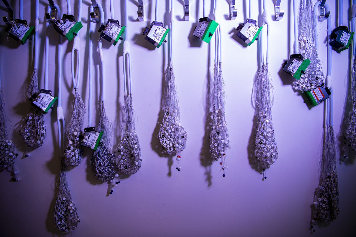 A row of caps with exposed wires and sensors used for cognitive tests hangs on the wall