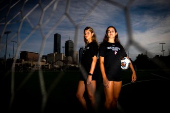 Two soccer players pose against a Boston skyline backdrop.