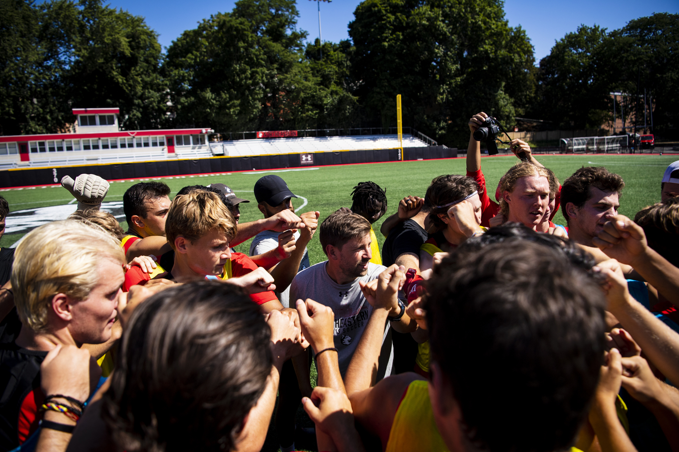 A group of soccer players stands together in a circle on a sports field.