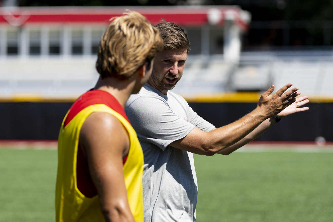 New men's soccer coach Richard Weinrebe (right) talks to a soccer player on a sports field. 