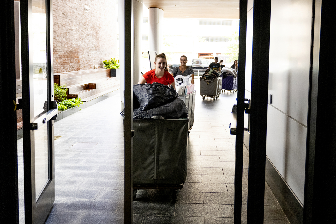 Four students line up outside a Northeastern dorm building with large hampers on wheels full of belongings to move into their rooms