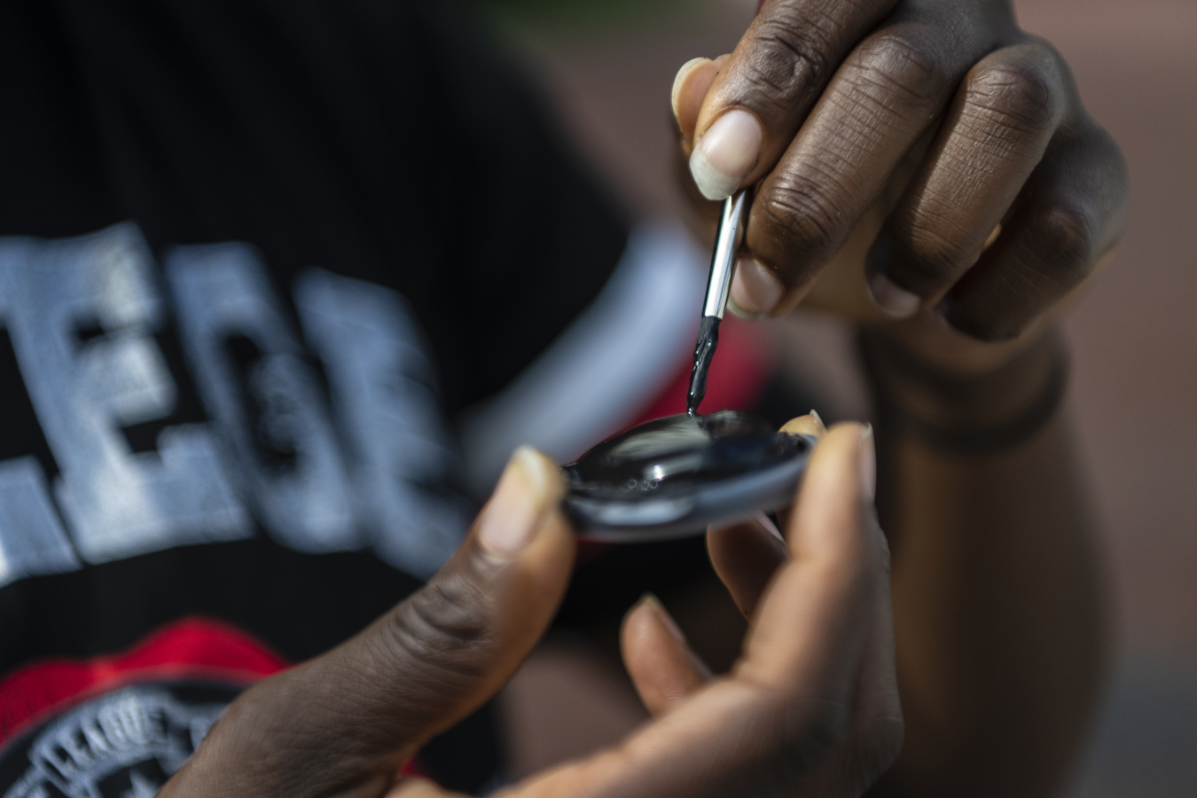 A hand dips a paintbrush into black paint. 