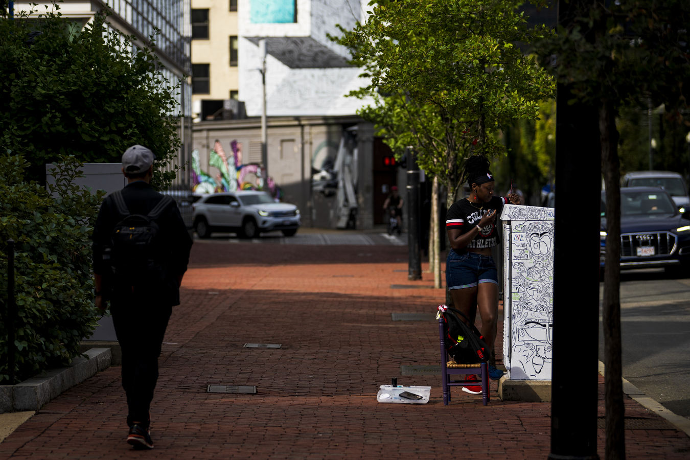 A person walks down a semi-bright sidewalk near multiple city buildings. 