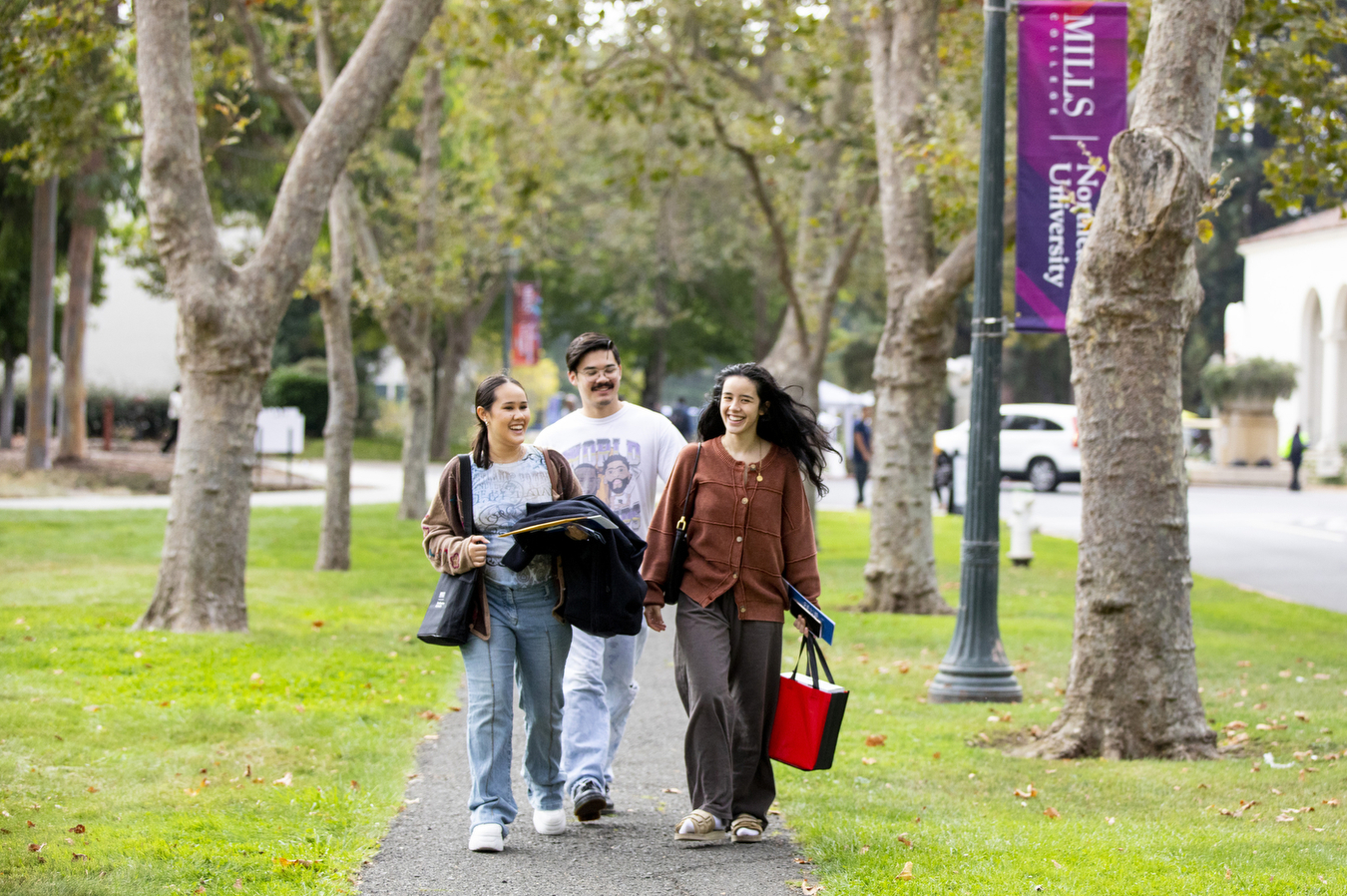 Three people walk down a tree-lined sidewalk smiling