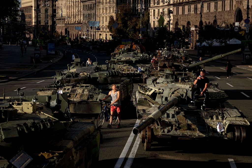 People walk among destroyed military vehicles on a city street