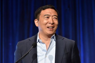 man standing in front of blue curtain wearing black suit jacket and light blue shirt