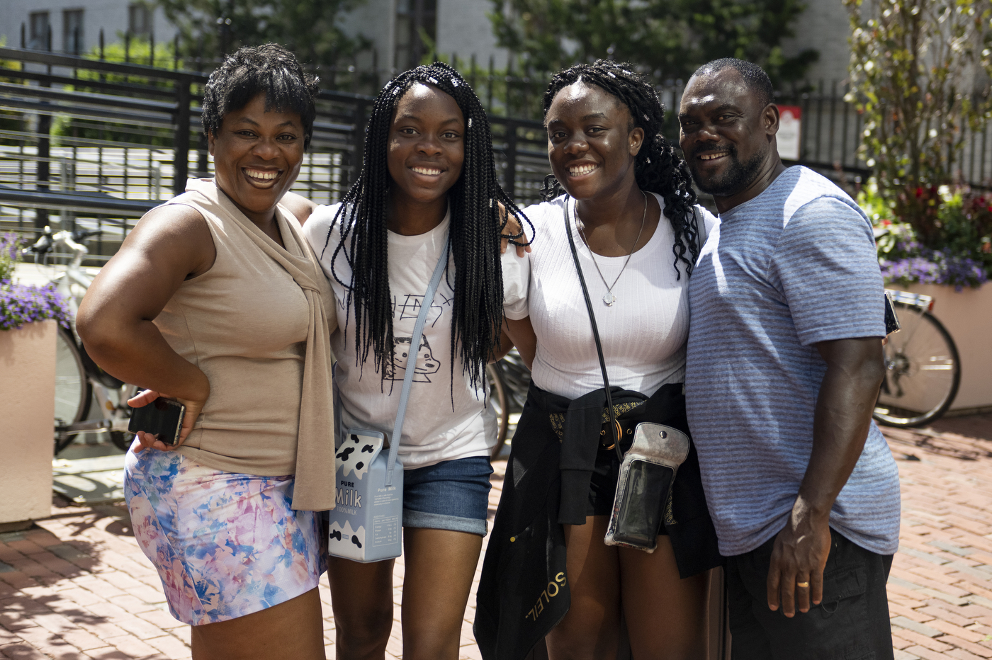 Parents of college students are smiling together with their children outside on a sunny day. 