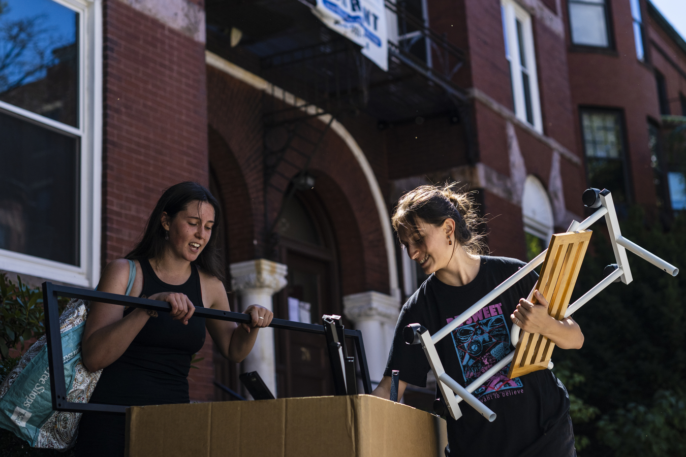 Two students unload personal items outside of a building. 