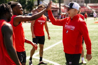 President Aoun (right) and a soccer player give each other a high five. Another soccer player is behind them on the field in the background.