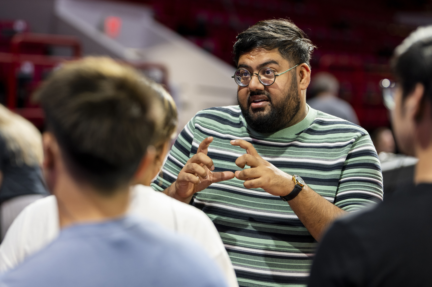 A person wearing a black, white, and light green shirt is talking to a crowd of people about Northeastern's Convocation.