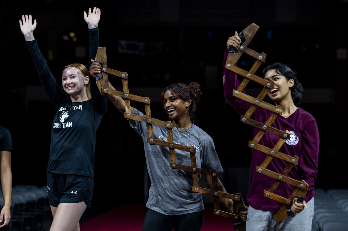 Three people are on stage, waving and holding large pieces of wood.