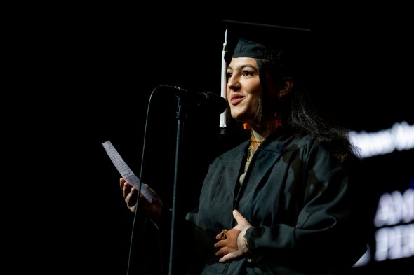 A person wearing a graduation cap and gown is talking into a microphone at Northeastern's 2022 Convocation.