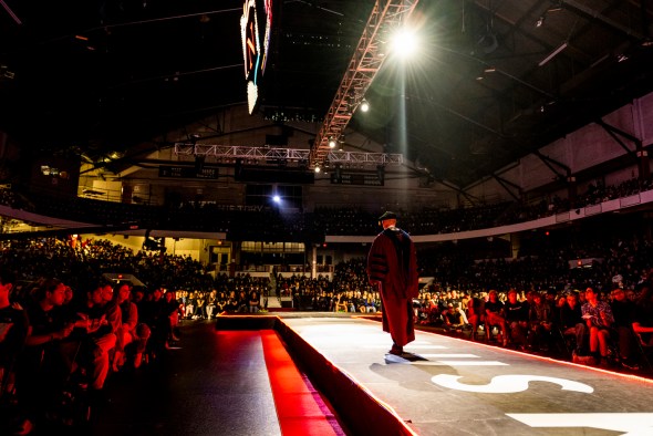 A person wearing a large red robe is walking down an aisle at Northeastern's 2022 Convocation.