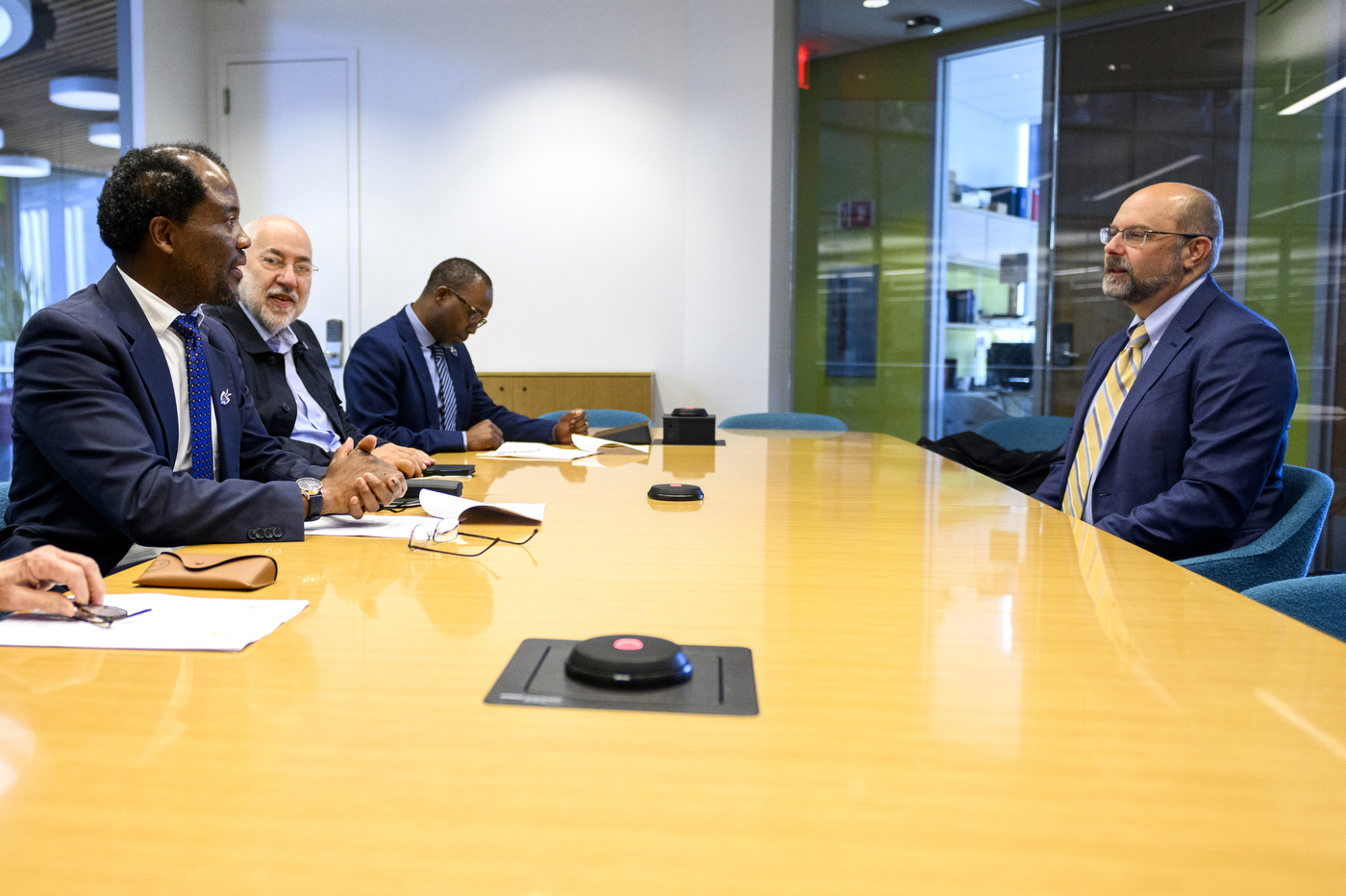 Men in blue and black suits sit together around a table to talk about Northeastern and Wits University. 