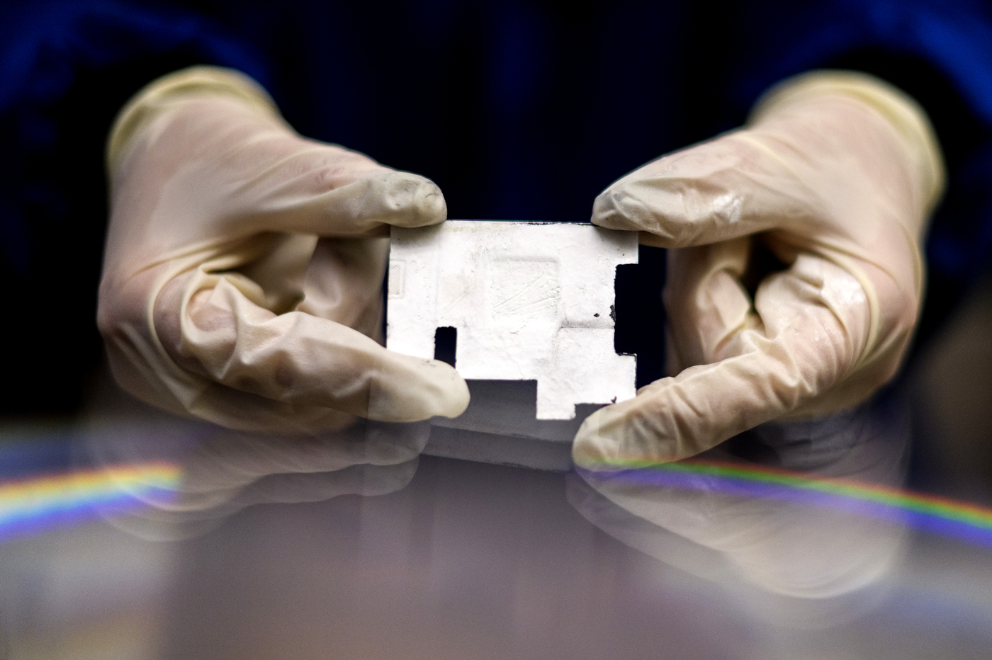 Two gloved hands holding a small ceramic component