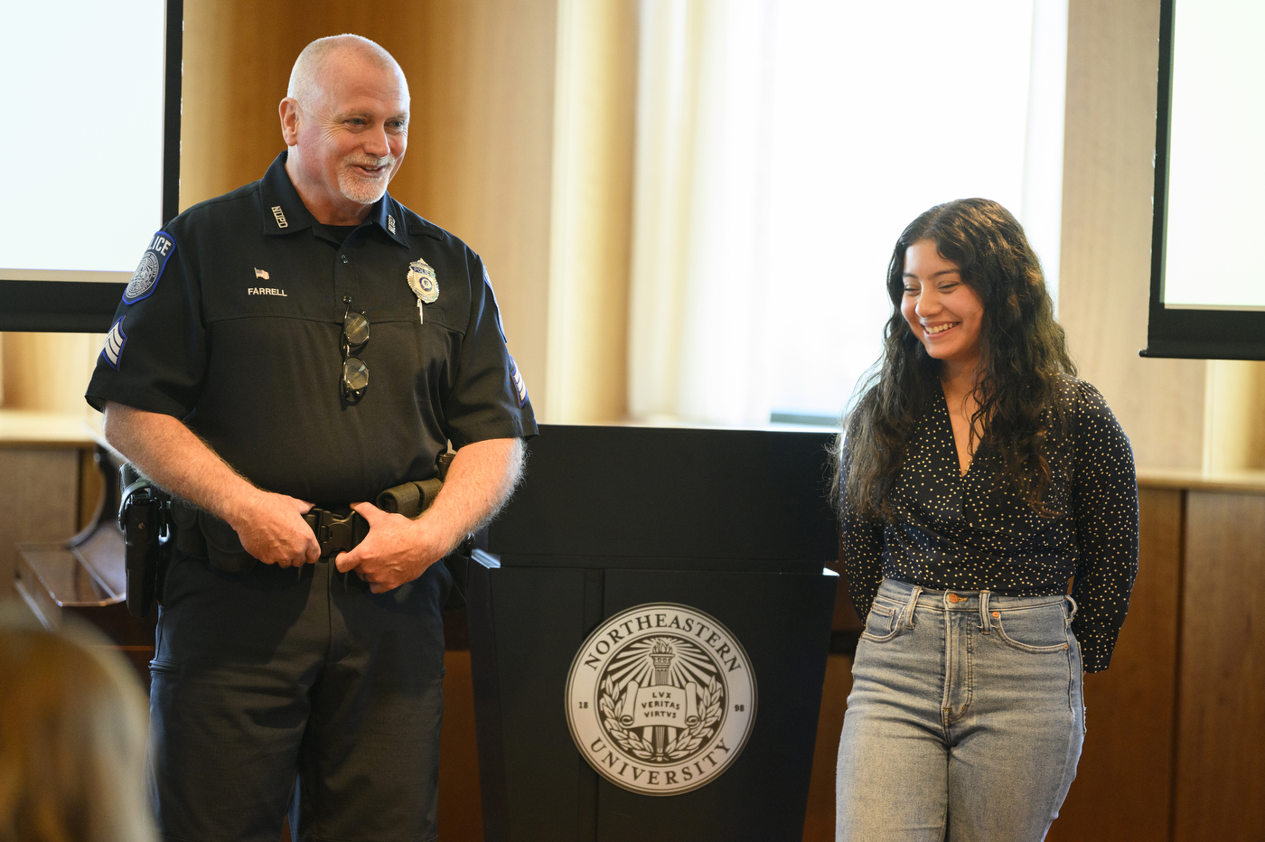 A police officer is standing next to a student part of their police mentorship program. 