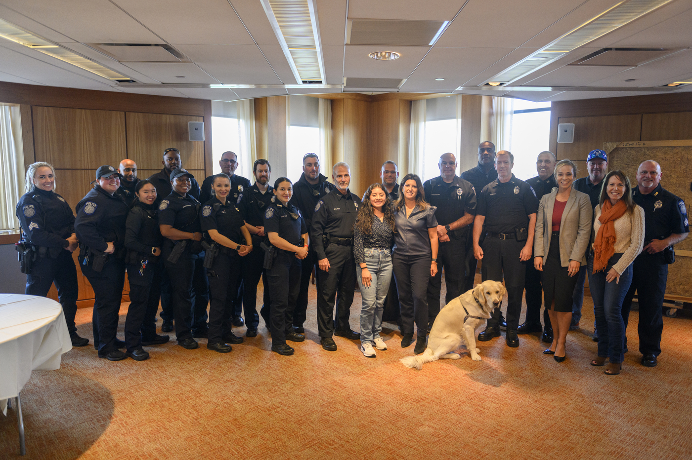 Multiple people wearing police uniforms are standing together in a brightly lit room for a police mentorship program. 